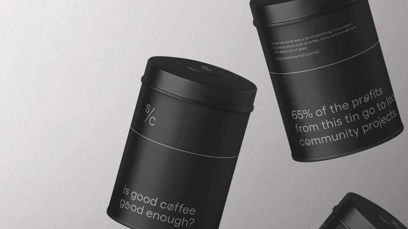 Three black tin coffee containers with branding labels, arranged on a light gray surface in a minimalist, product-focused composition.