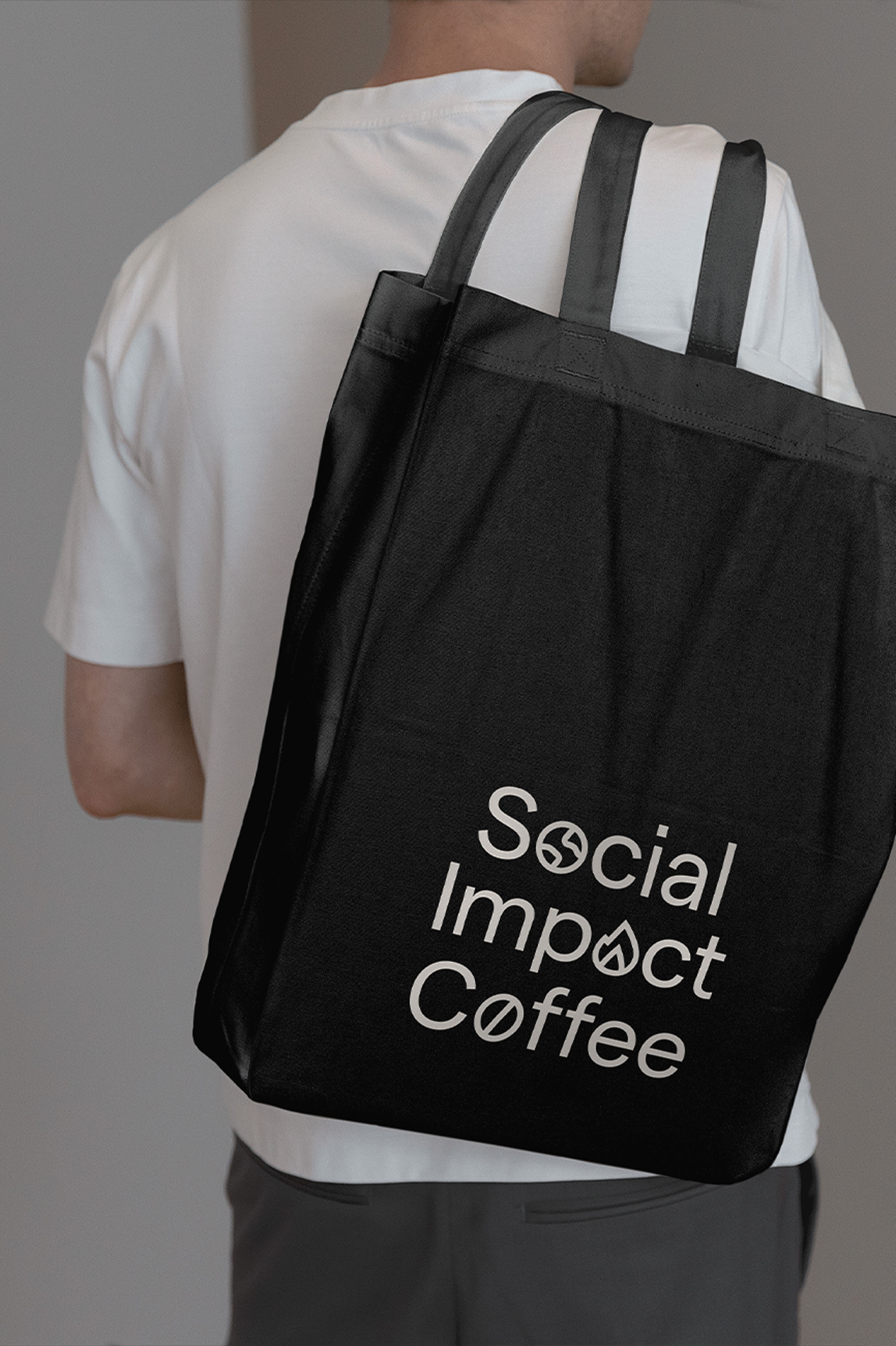 Person carrying a black tote bag with the text 'Social Impact Coffee' printed in white. Minimalist shot.
