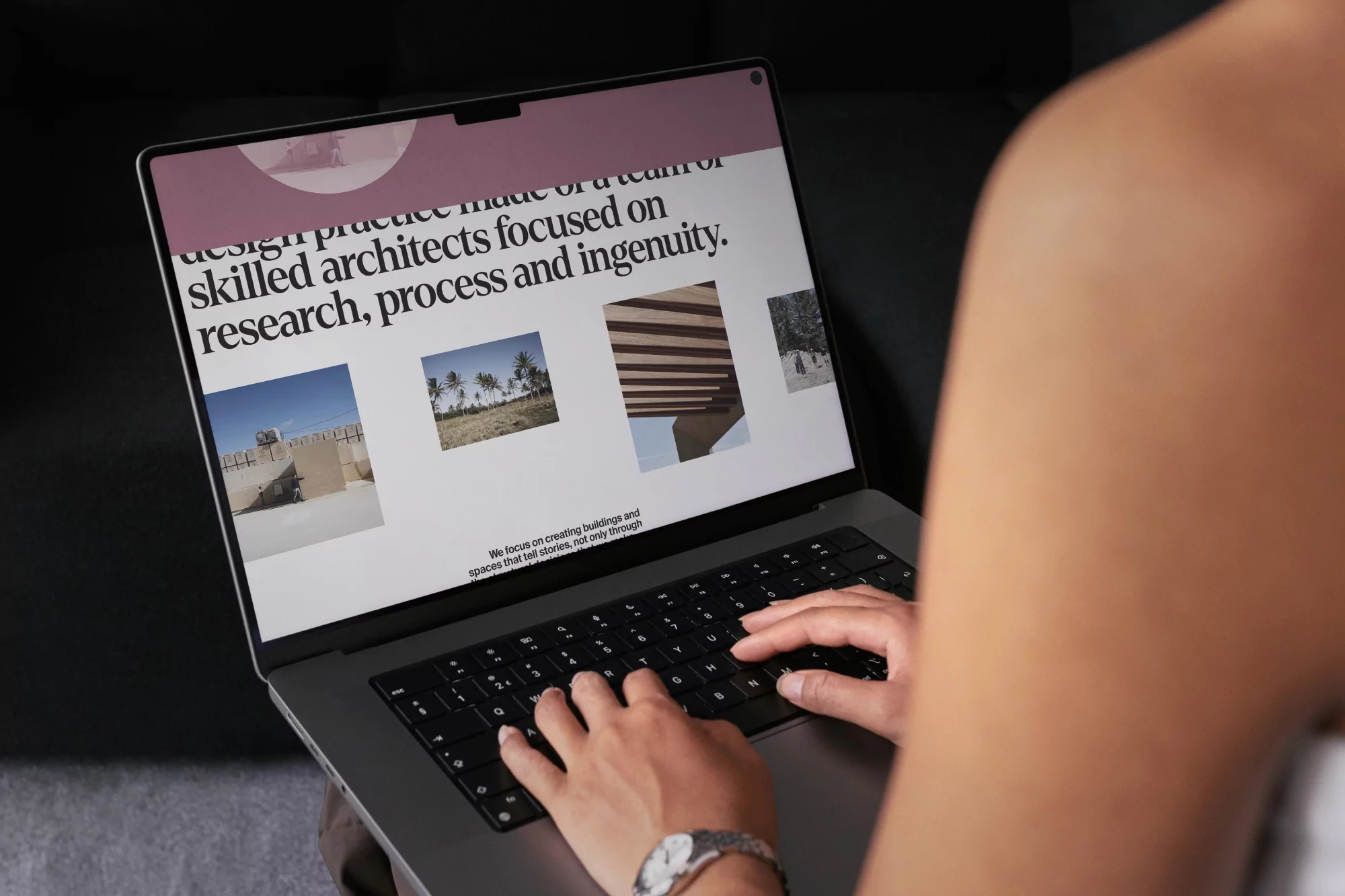 Woman types on a laptop displaying a website with architectural images in a home interior. The laptop is gray with black keys.