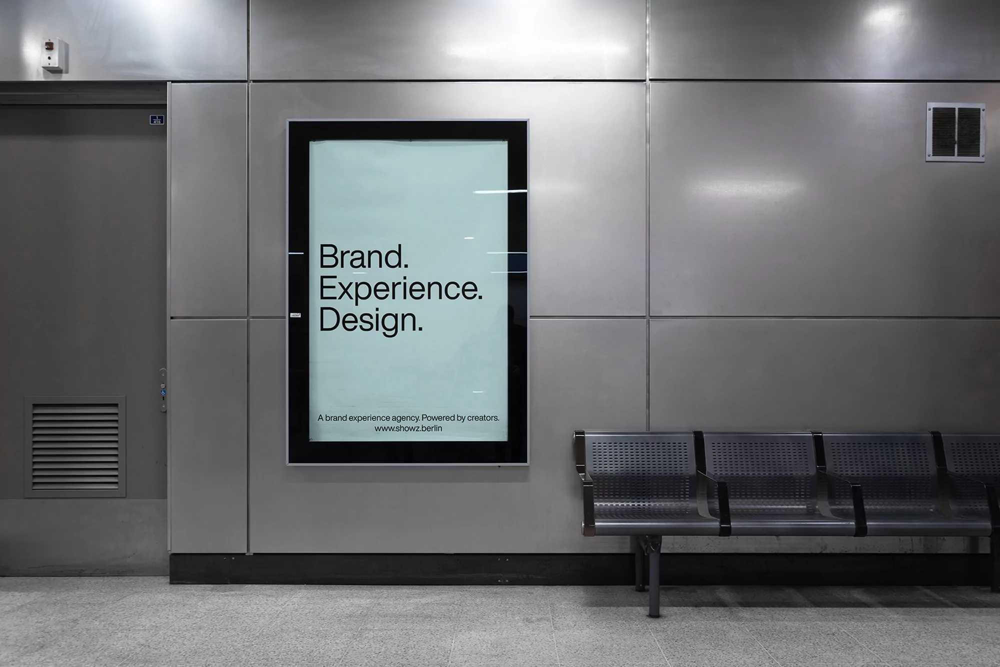 Illuminated advertising display showcasing 'Brand. Experience. Design.' in a modern urban setting with metallic bench seating.