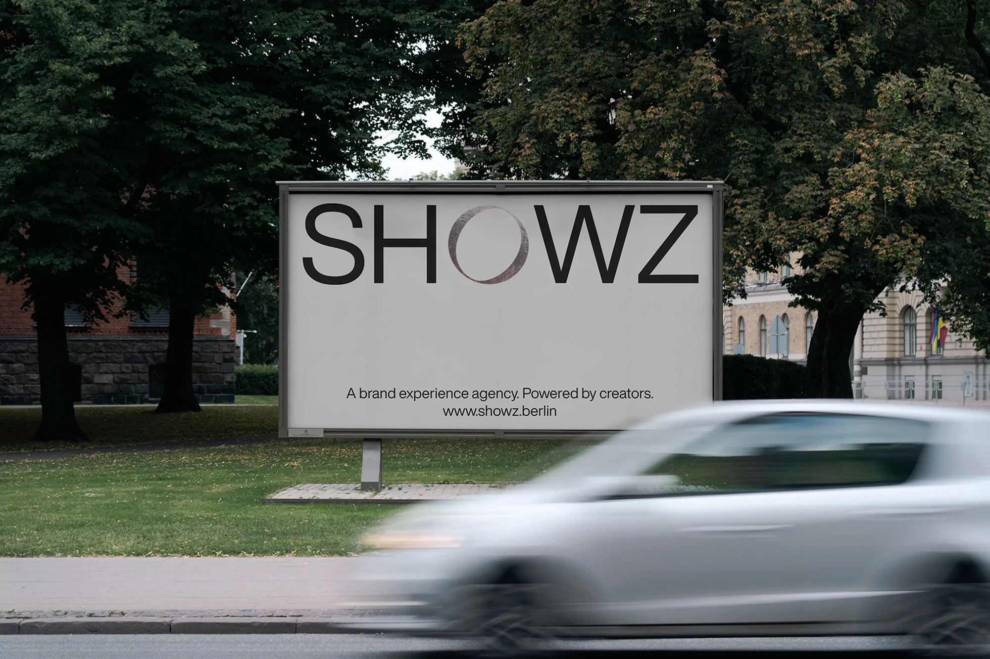 Outdoor billboard with 'SHOWZ' text, advertising a brand experience agency, set against a backdrop of green trees and urban architecture.