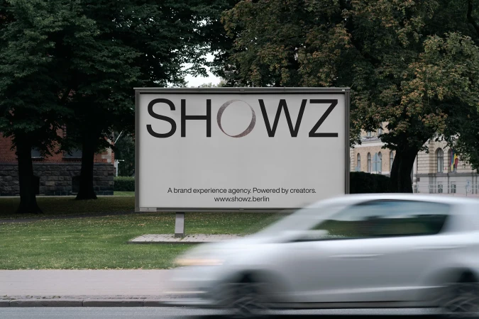 Outdoor billboard with 'SHOWZ' text, advertising a brand experience agency, set against a backdrop of green trees and urban architecture.