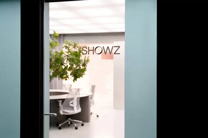 Office space featuring a conference table and office chairs viewed through an open doorway with the brand logo on the door.