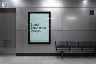 Vertical digital billboard on a metallic wall next to empty metal bench seating in an indoor transit or terminal station