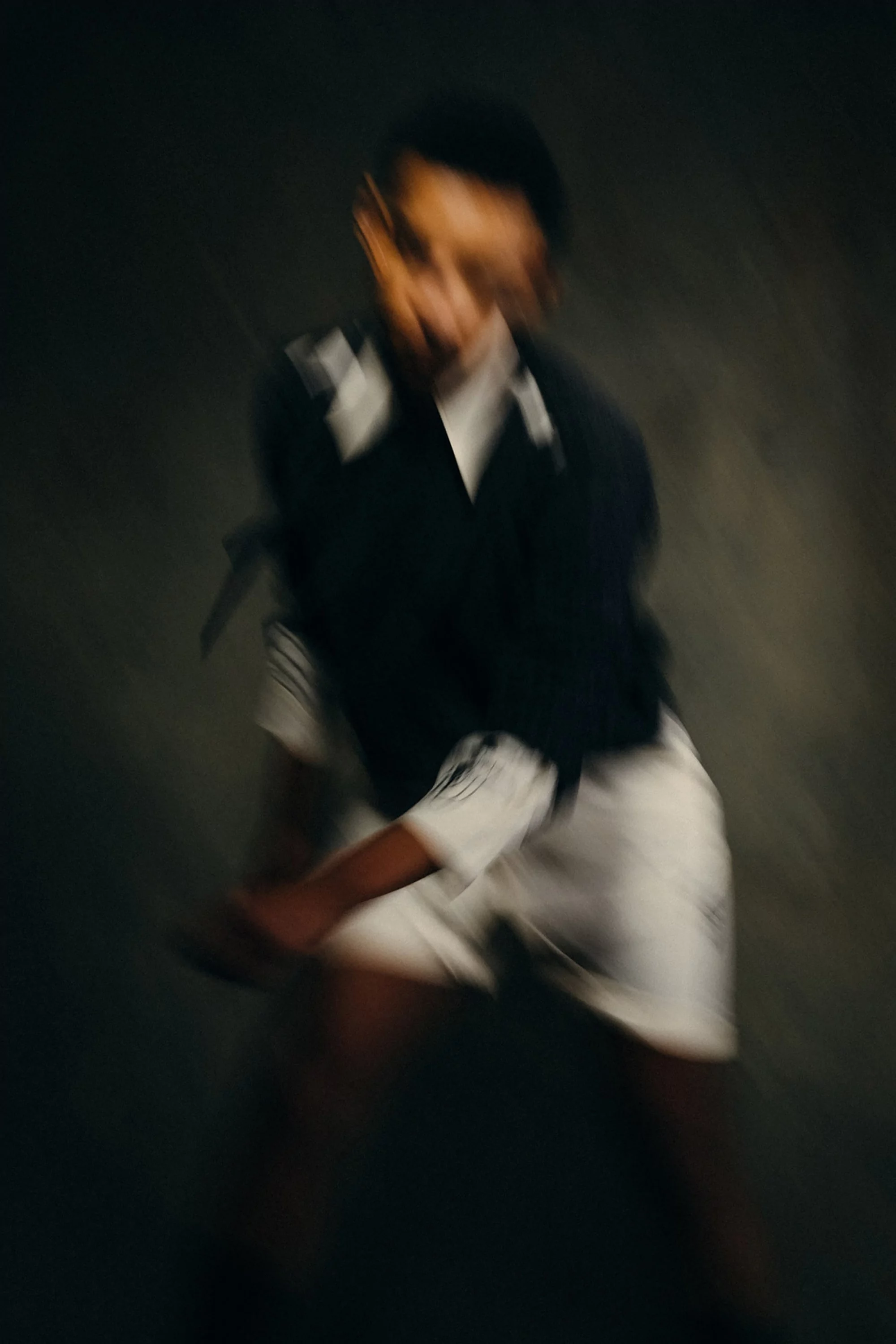 Motion blur studio shot of a Black adult in a black and white athletic outfit. Athletic figure in a studio environment with dark backdrop.