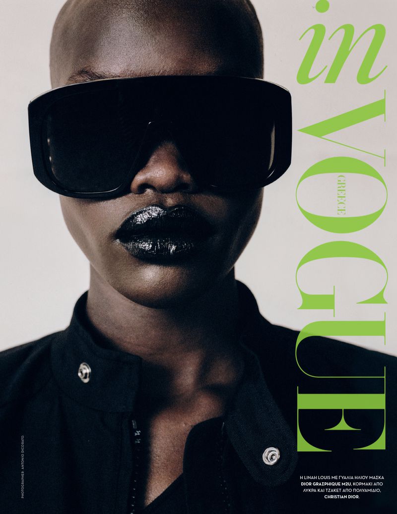 Close-up fashion shot of bald African woman wearing oversized black sunglasses and glossy dark lipstick for In Vogue Greece magazine.
