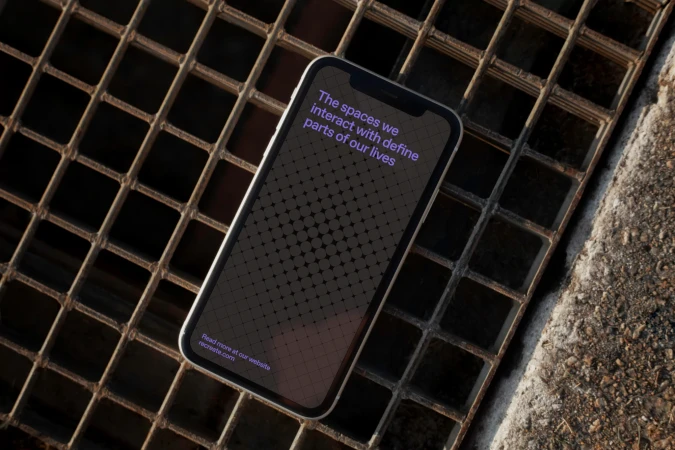 Mobile phone displaying an app with text on a metal grate. Modern smartphone presents text overlay and website on a gray background.