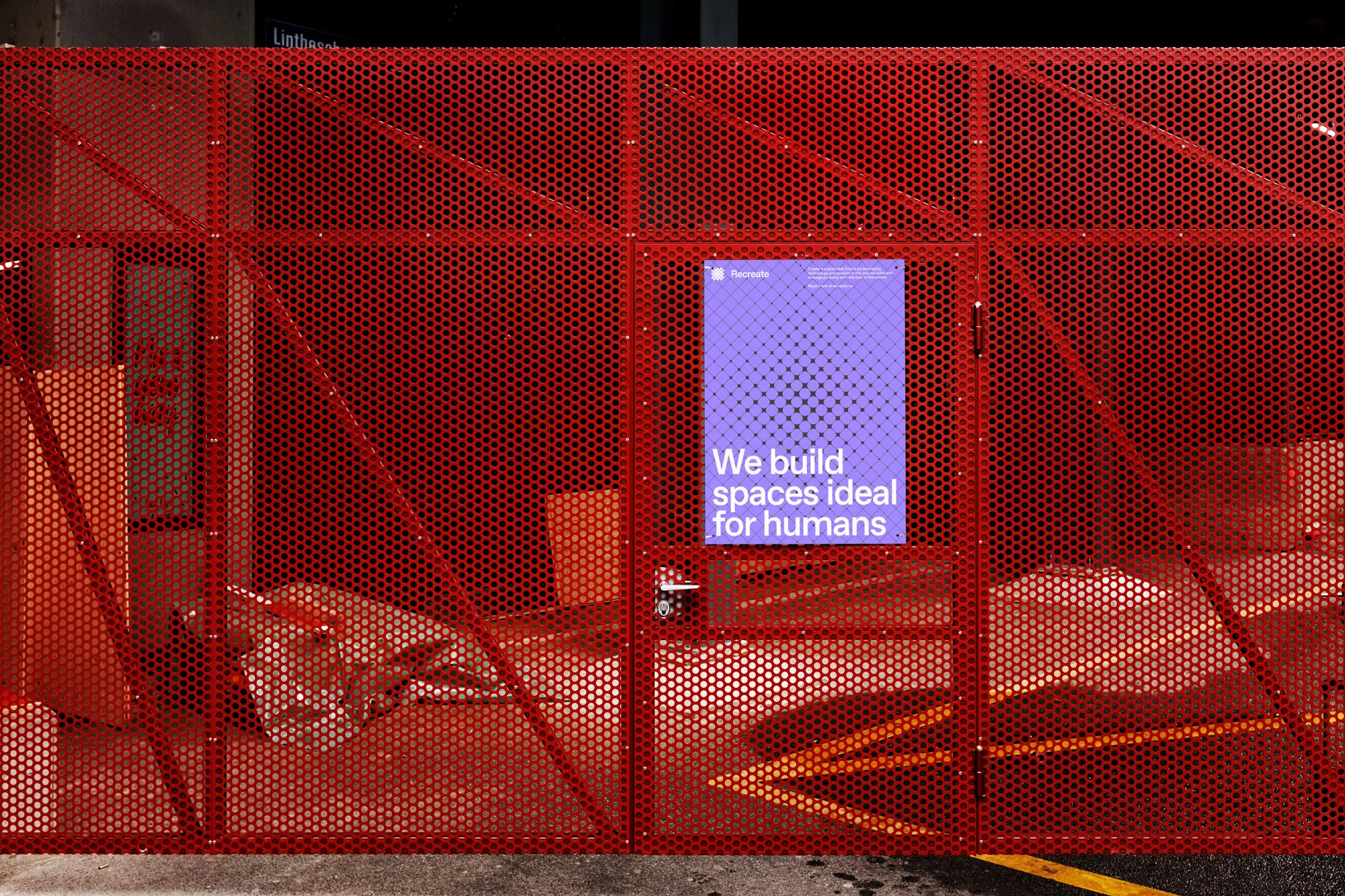 Red metal mesh fence with a purple sign that reads, 'We build spaces ideal for humans.' Visible are construction materials.