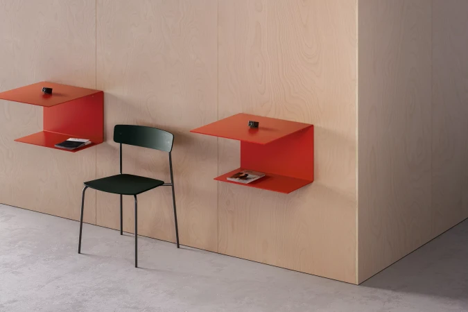 Interior design featuring minimalist furniture: red floating shelves with small objects and a green chair against a light wood wall.