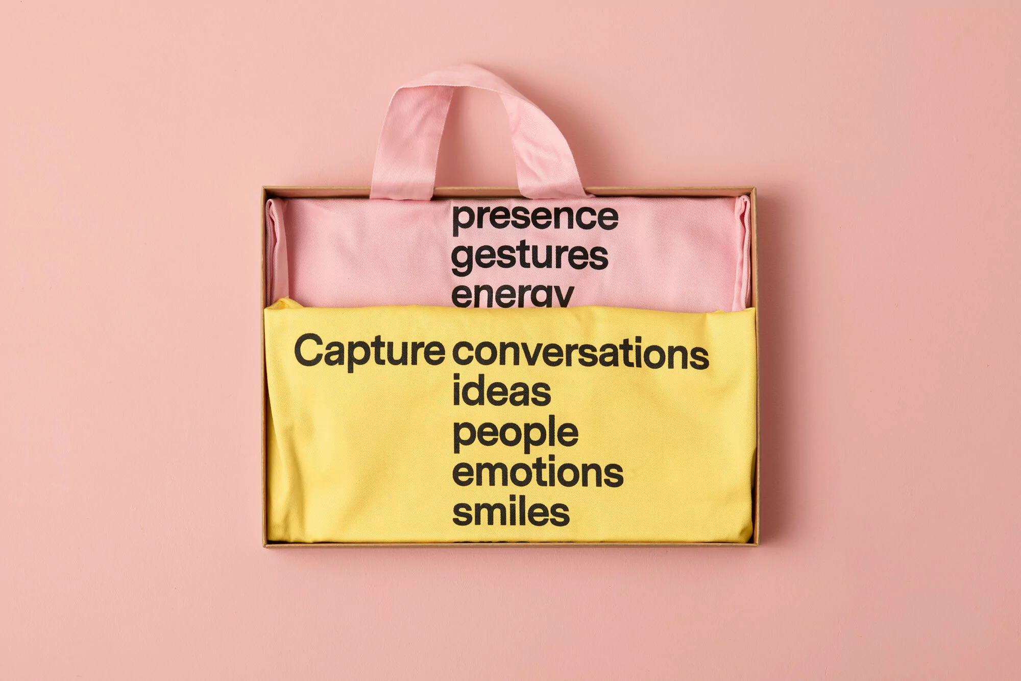 Box with pink and yellow fabric, featuring black text on both layers, set against a peach-colored backdrop in a studio shot.