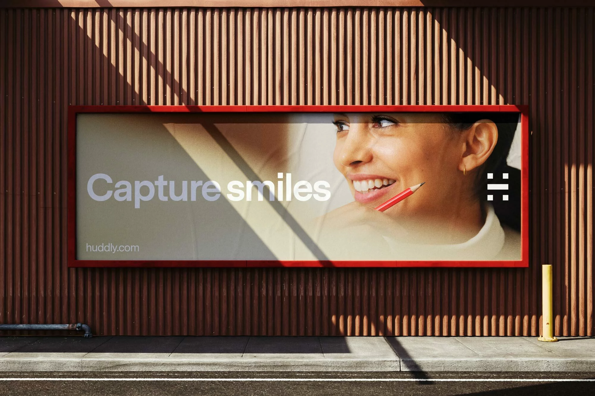 Outdoor advertising billboard featuring a smiling woman holding a red pencil, displayed against a brown corrugated wall.