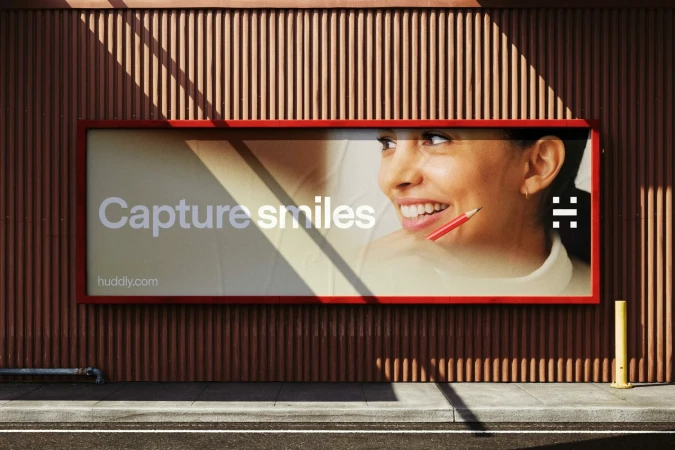 Outdoor billboard displaying a Huddly brand advertisement on a ribbed brown metal wall