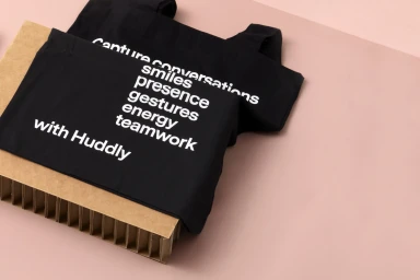 Black fabric bags with white text displayed on brown corrugated paper against a solid pink surface