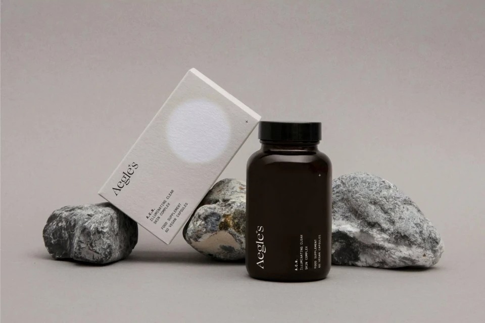 Brown supplement bottle and product box with Aegle's logo displayed on gray rocks against a grey background in a studio shot.