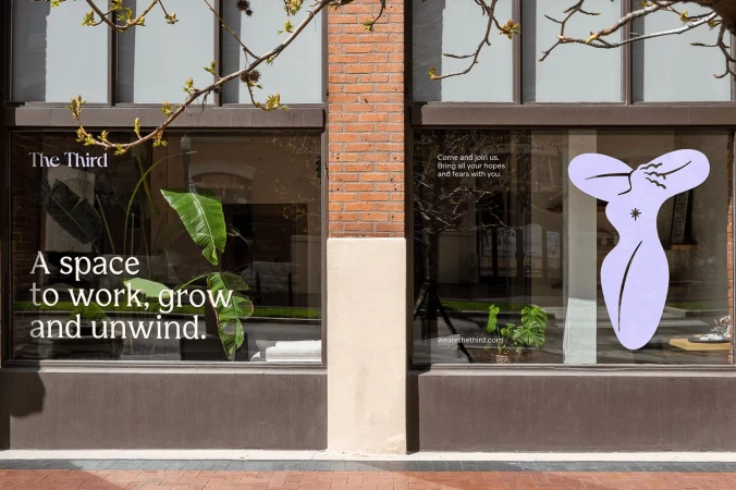 Exterior of a business, The Third, featuring window graphics, indoor plants, and minimalist interior design elements, during daylight.