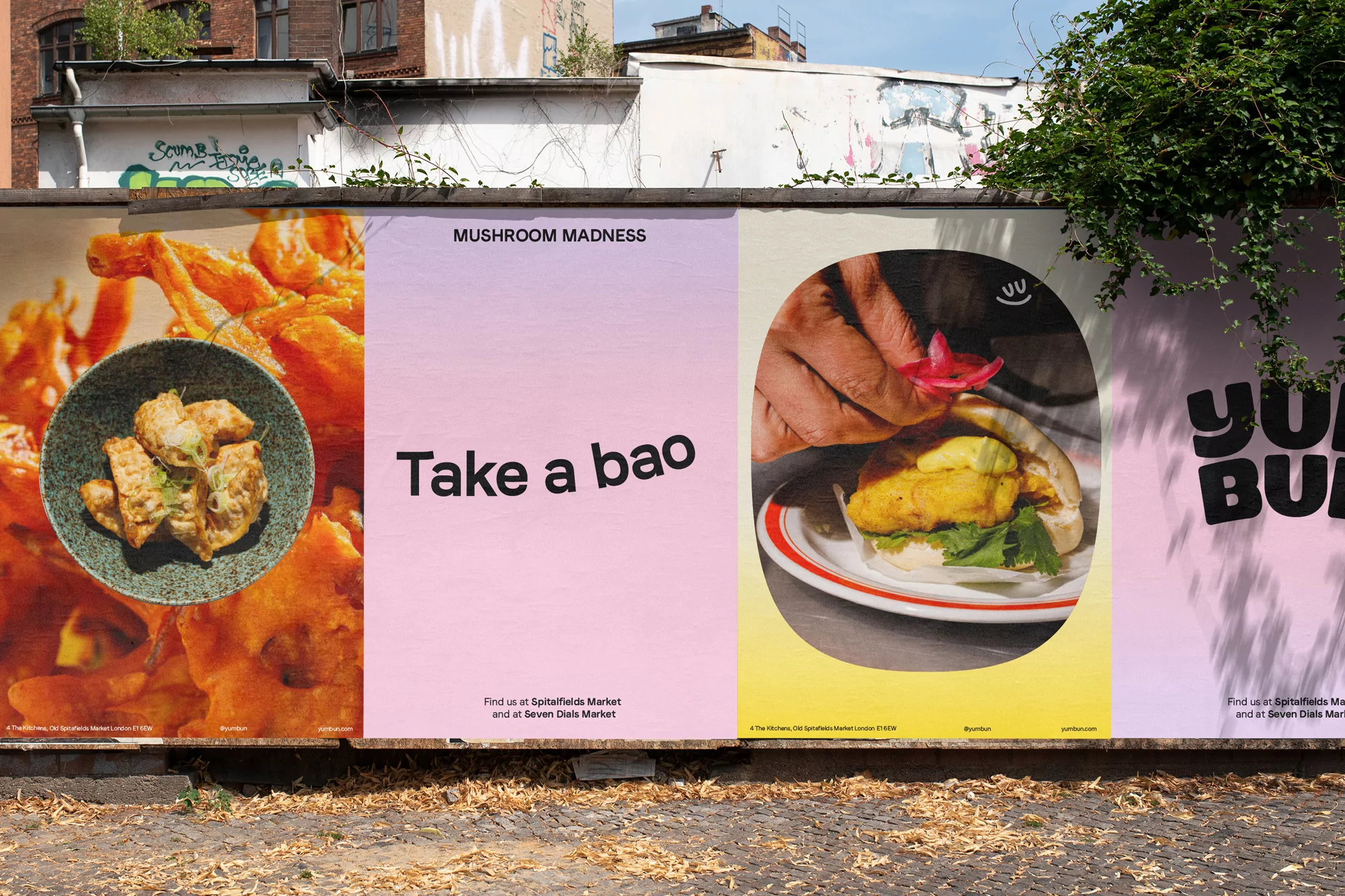 Food posters of mushroom bao buns and fried shrimp displayed on an outdoor wall with greenery, promoting Spitalfields Market.