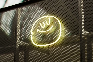 Glowing yellow neon smiley face sign mounted on a dark perforated metal surface for Yum Bun brand identity design.