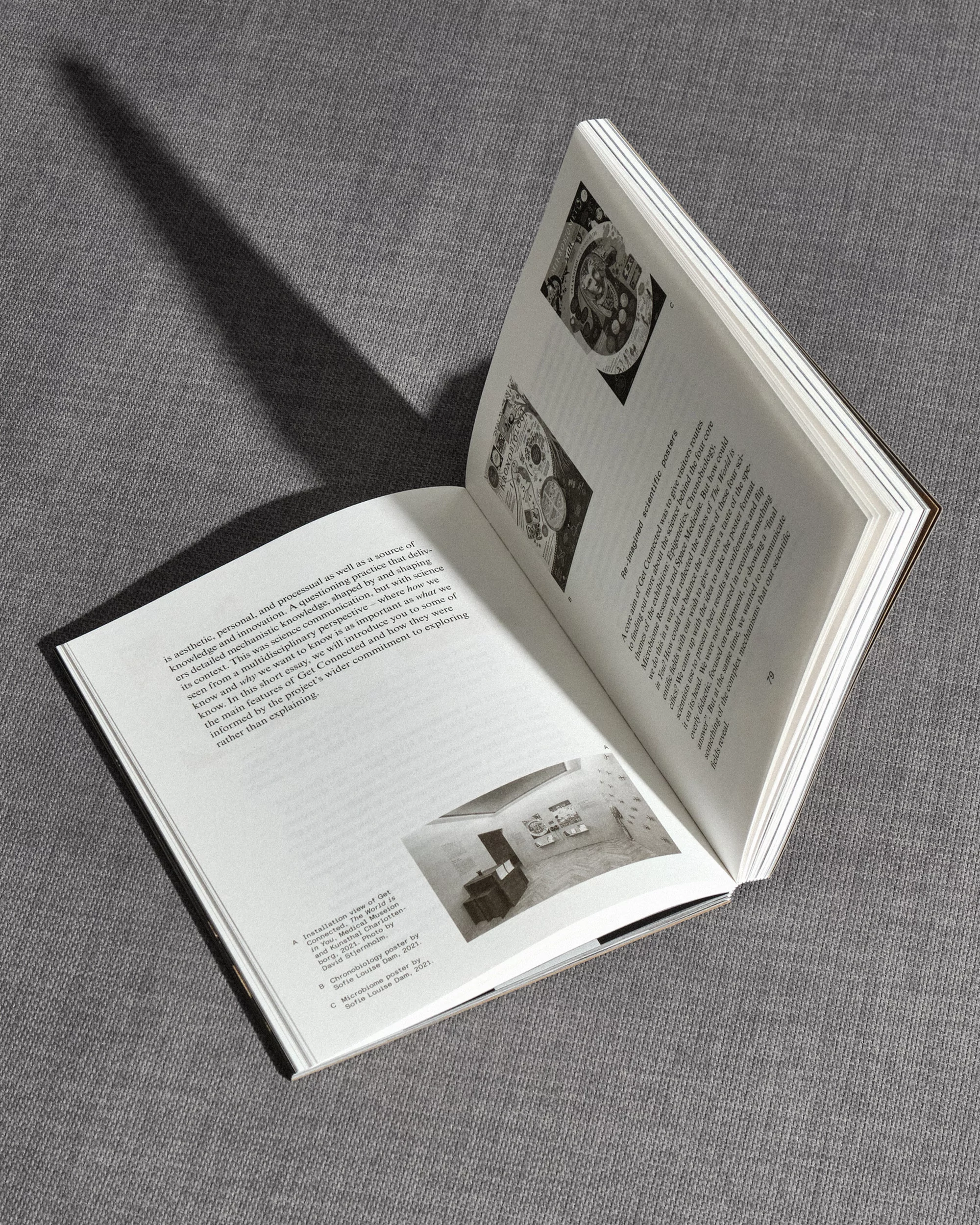 Open book with architectural photography and text on textured gray background, illuminated by a shadow, showcasing interior design.