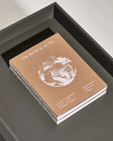 Close-up of a brown cover book on a dark gray tray, featuring a white earth graphic and the text 'The World is in You'.