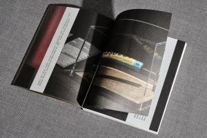 An open book displaying black pages with photographs of museum exhibits resting on a textured grey fabric surface.