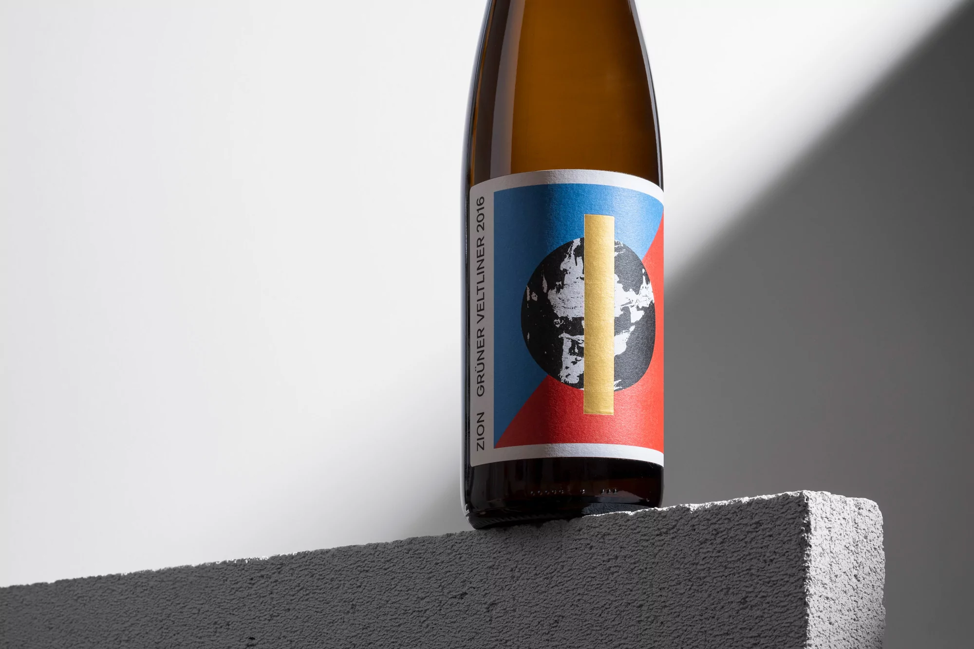 Close-up of a bottle of Grüner Veltliner wine with a minimalist label featuring a blue, red, and black globe design.