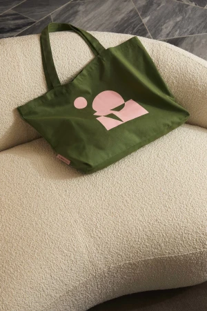 Olive green tote bag with pink graphic logo on a textured beige couch. Fashionable and sustainable accessory for everyday use.