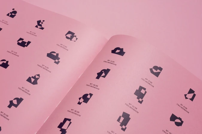 Open book pages filled with geometric abstract art and typography on a pink background, showing architectural plans and designs.