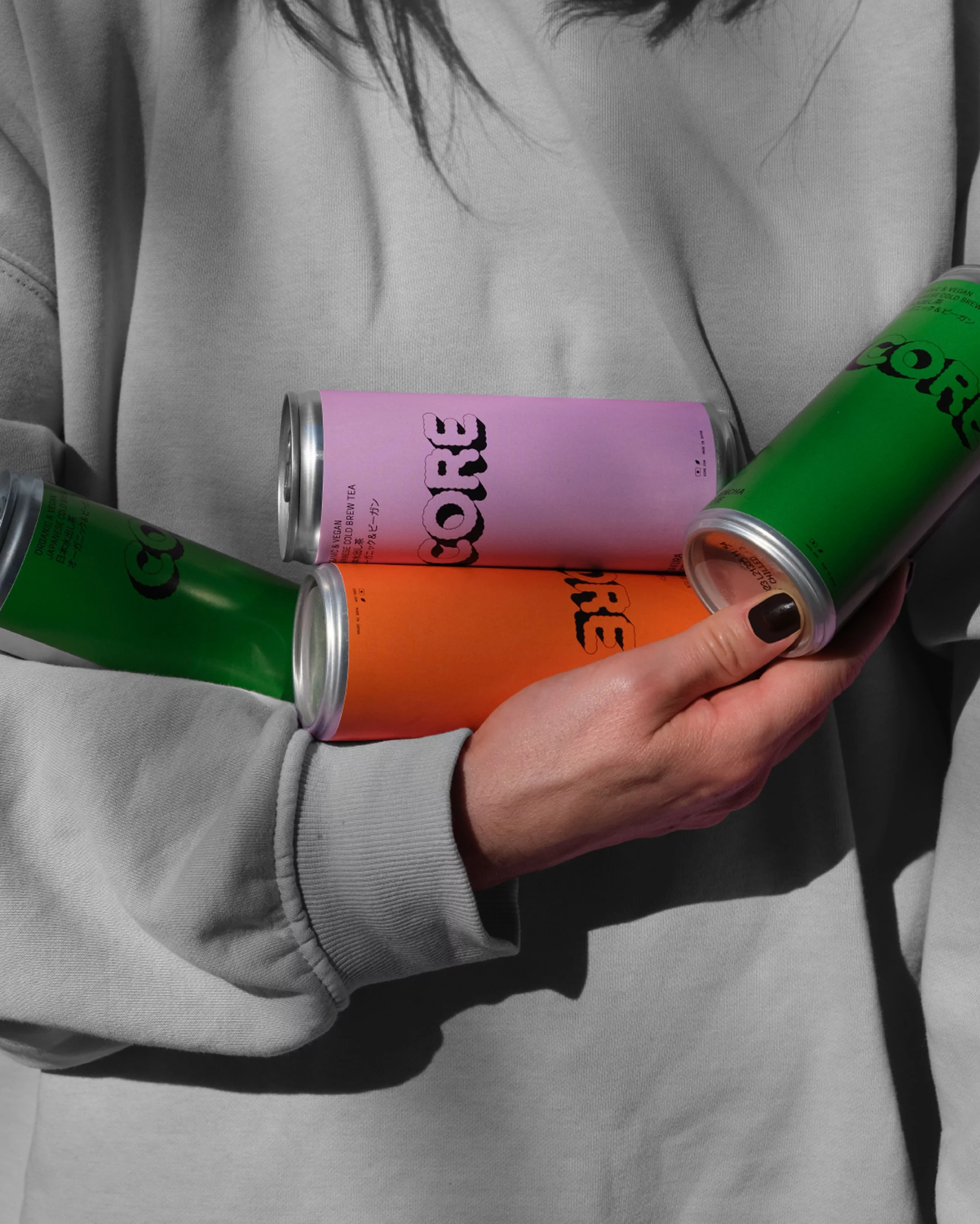 A person holds four colorful CORE brand drink cans in hues of green, orange, and lavender, showcasing beverage products.