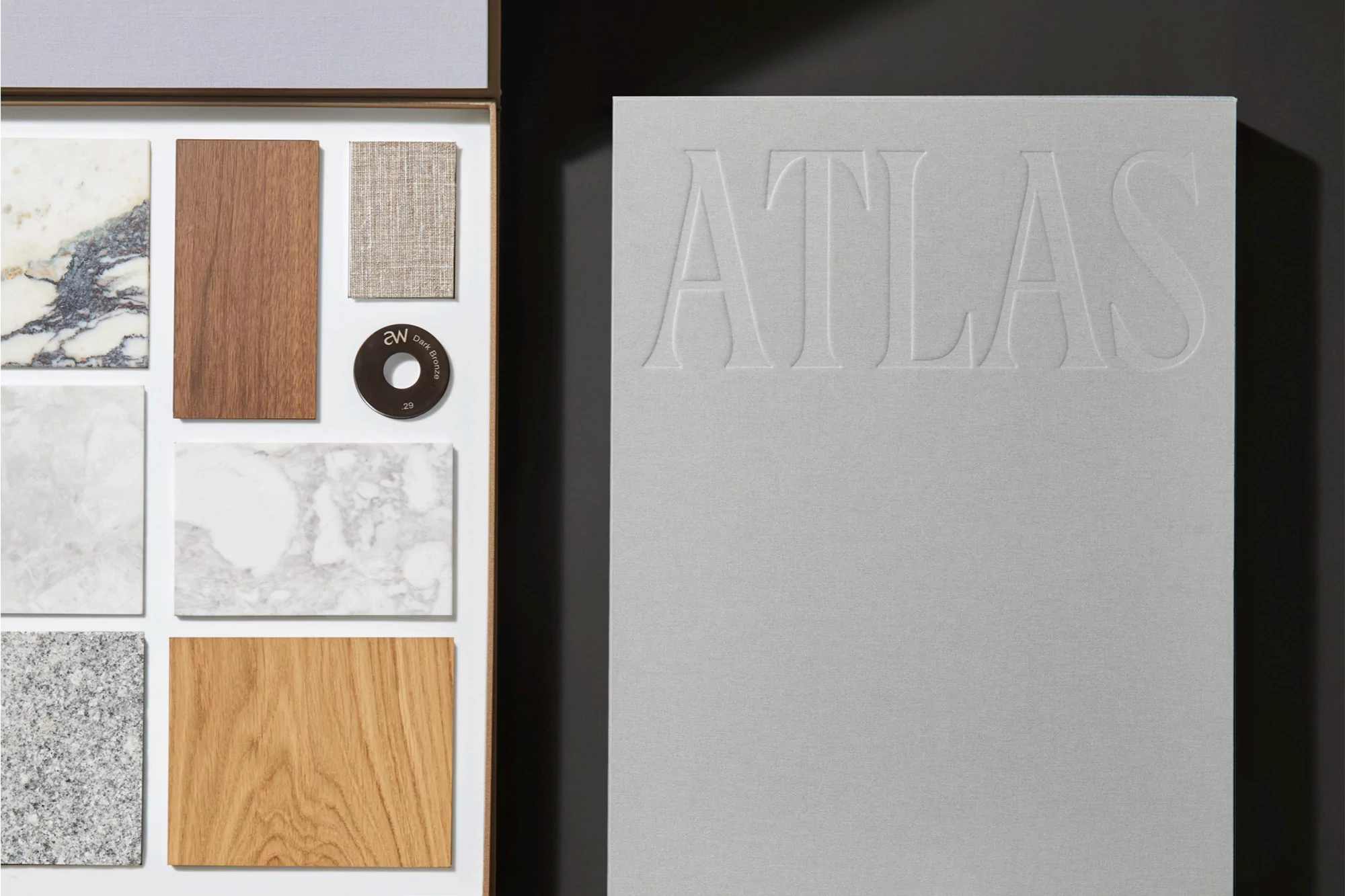 Interior design material samples and Atlas book on a dark background with natural textures and a light gray color palette.