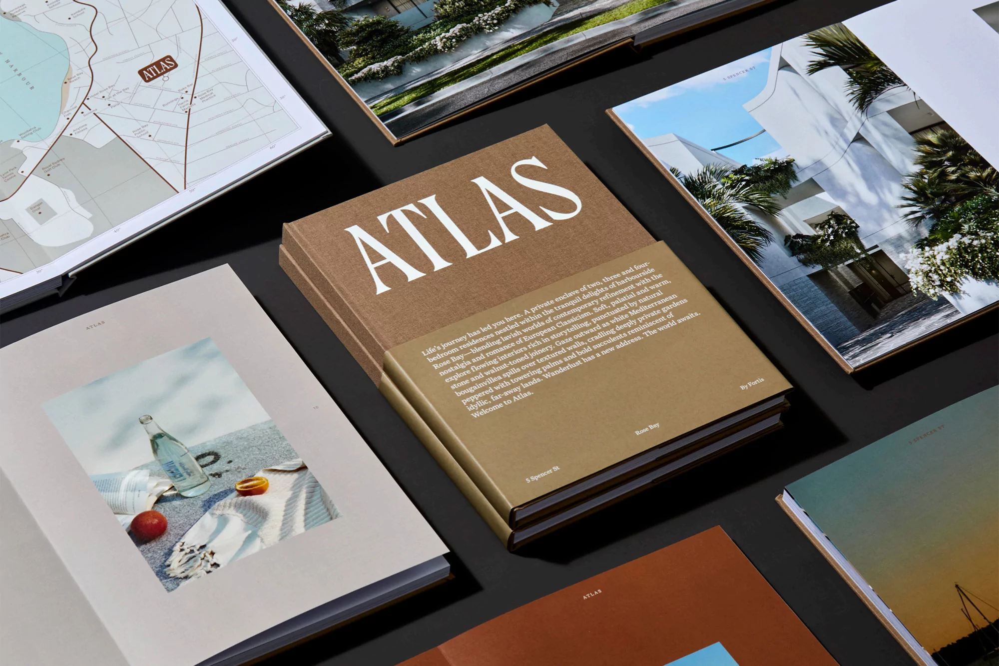 Promotional shot of a hardcover 'Atlas' book with a beige and white cover, surrounded by interior design and map photography books, studio setting.