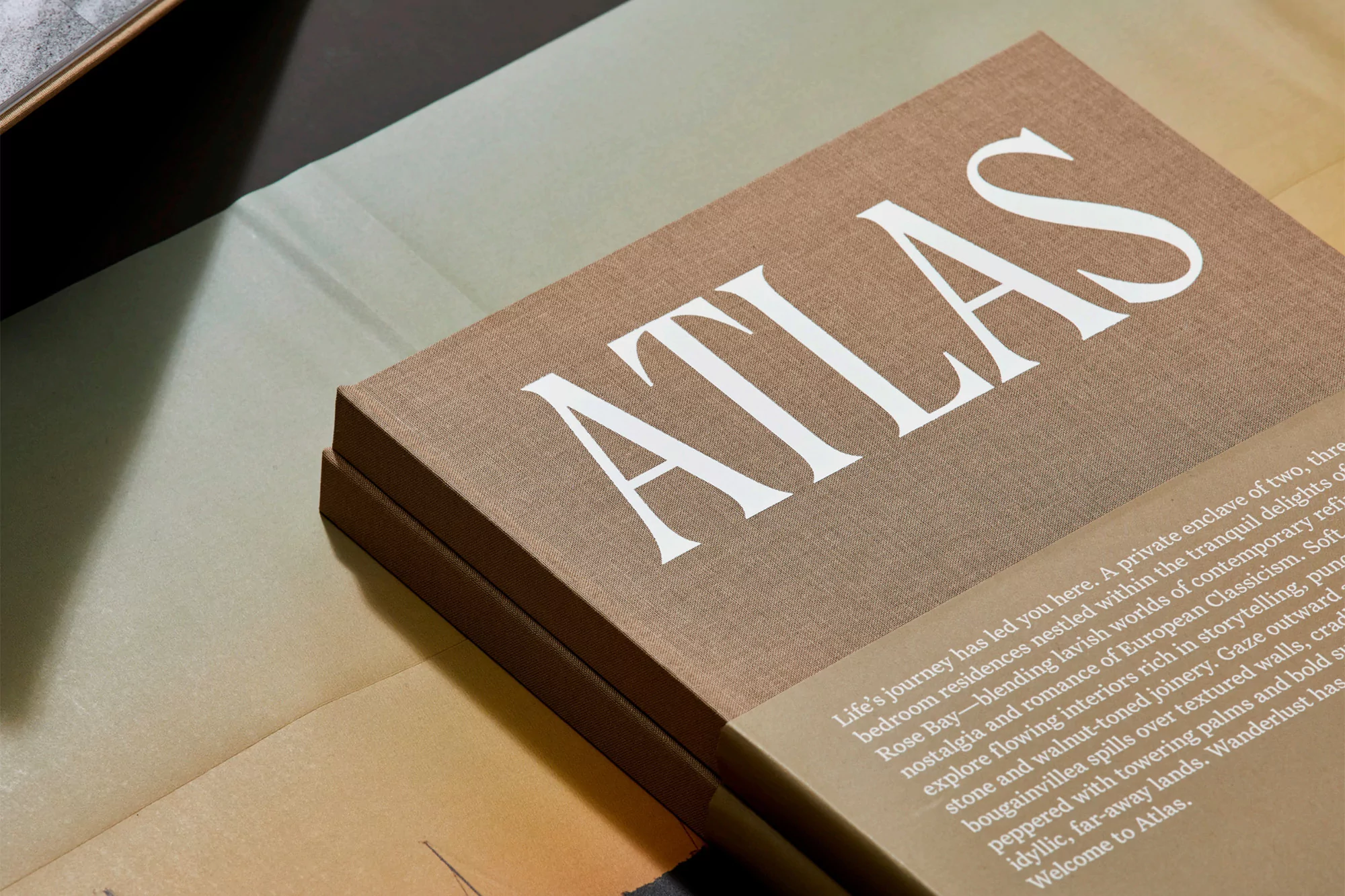 Close-up of an Atlas book with white font, placed on top of other books. The book has a brown cover and has some text on it.
