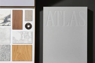 Material samples box with marble, wood, and fabric swatches next to a grey book with Atlas embossed on the cover.