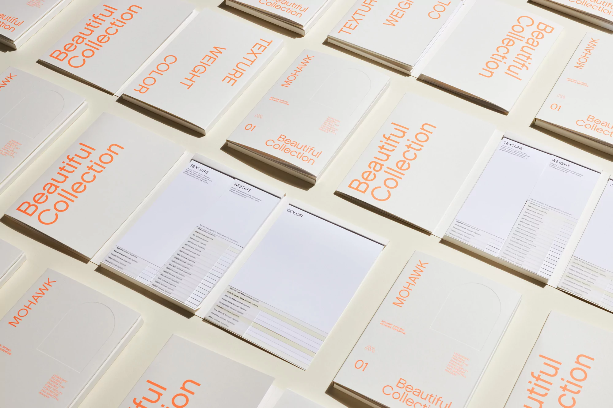 Multiple Mohawk paper sample books are displayed in a grid pattern, showcasing their texture, weight, and color options for designers.