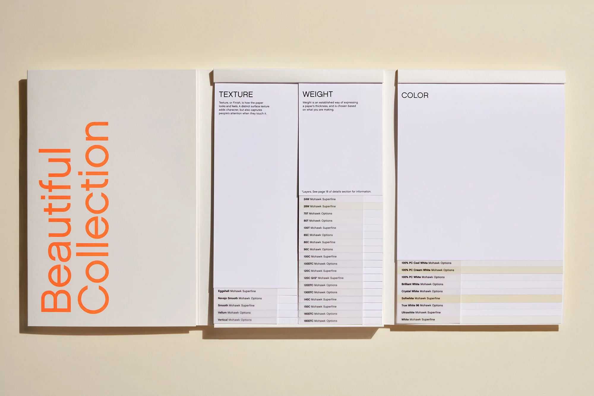 Paper swatches from the Beautiful Collection showing texture, weight, and color options, lying on a cream surface in bright studio lighting.