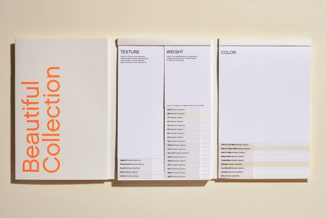 Paper swatches from the Beautiful Collection showing texture, weight, and color options, lying on a cream surface in bright studio lighting.
