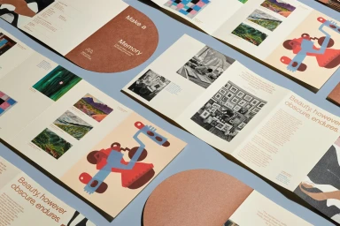 Open printed brochures with art illustrations and typography laid out on a light blue surface