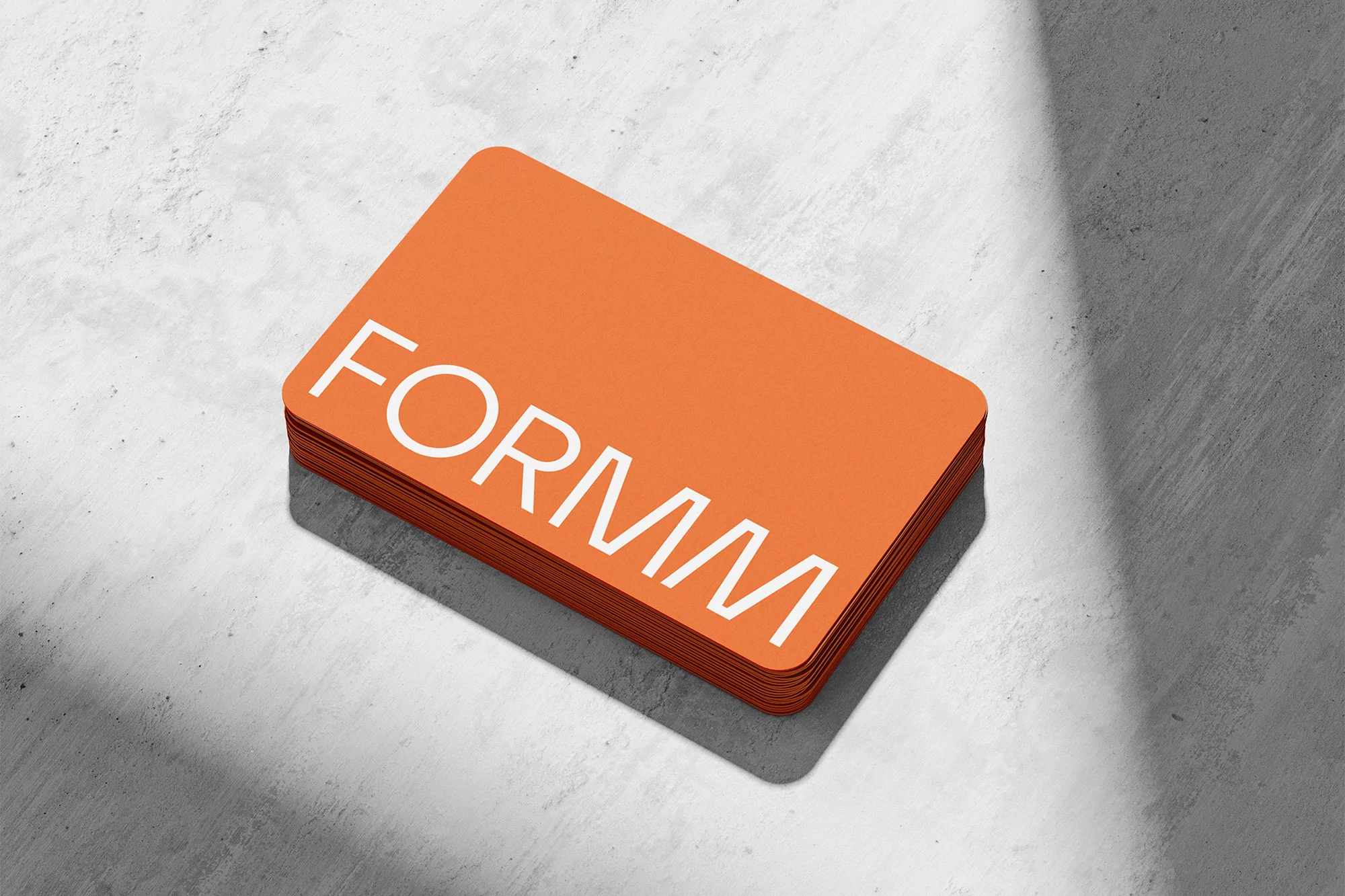 A stack of vibrant orange business cards featuring the white FORMM logo, placed on a textured grey concrete surface.