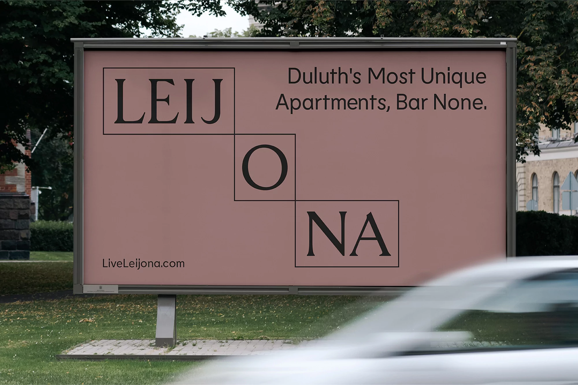Billboard in outdoor setting displays large text ad for Leijona apartments, framed by green trees and hint of building. Car passes in foreground.