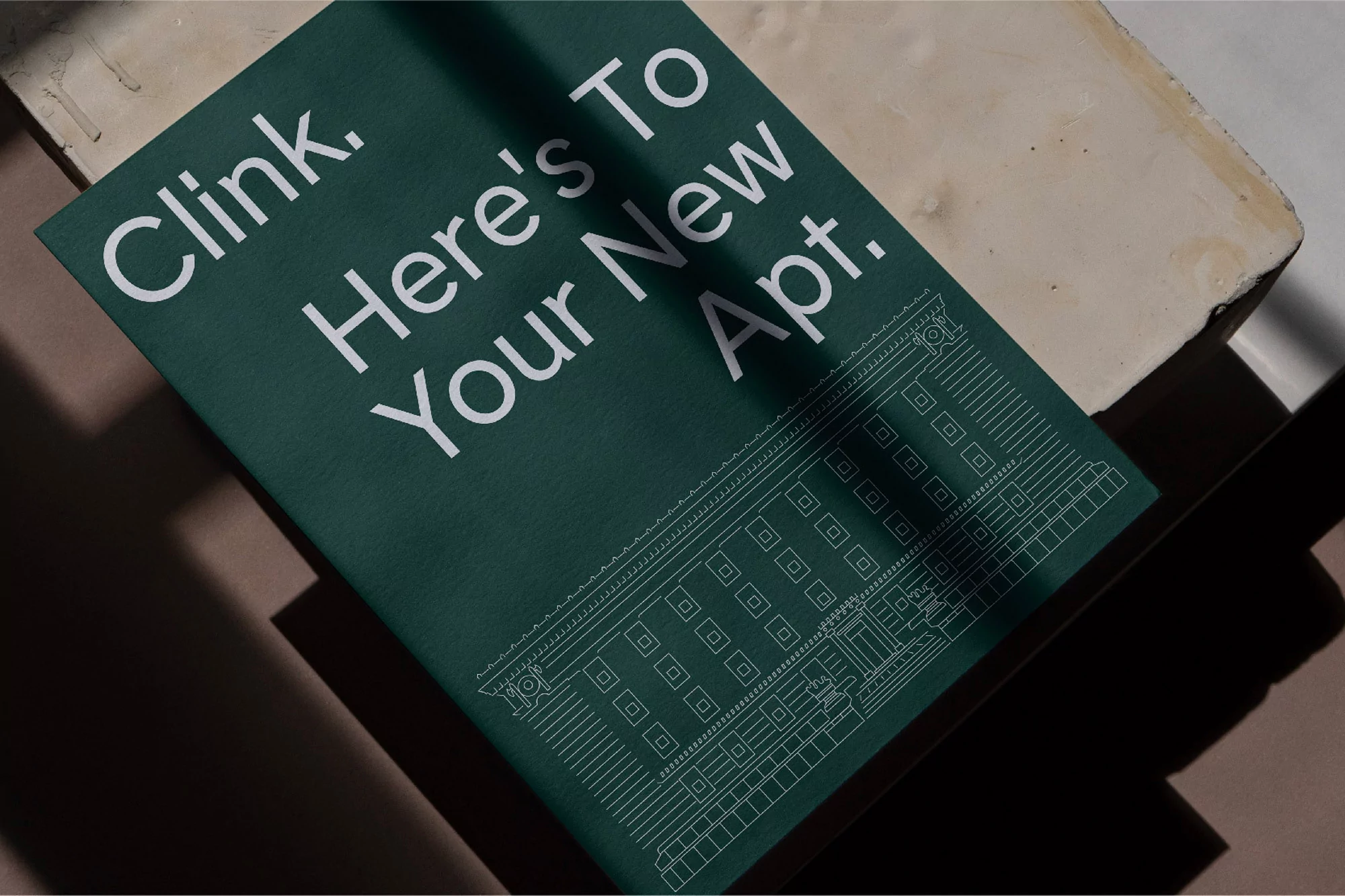 Close-up of a green book titled 'Clink. Here's To Your New Apt.' with a white line drawing of an apartment building.
