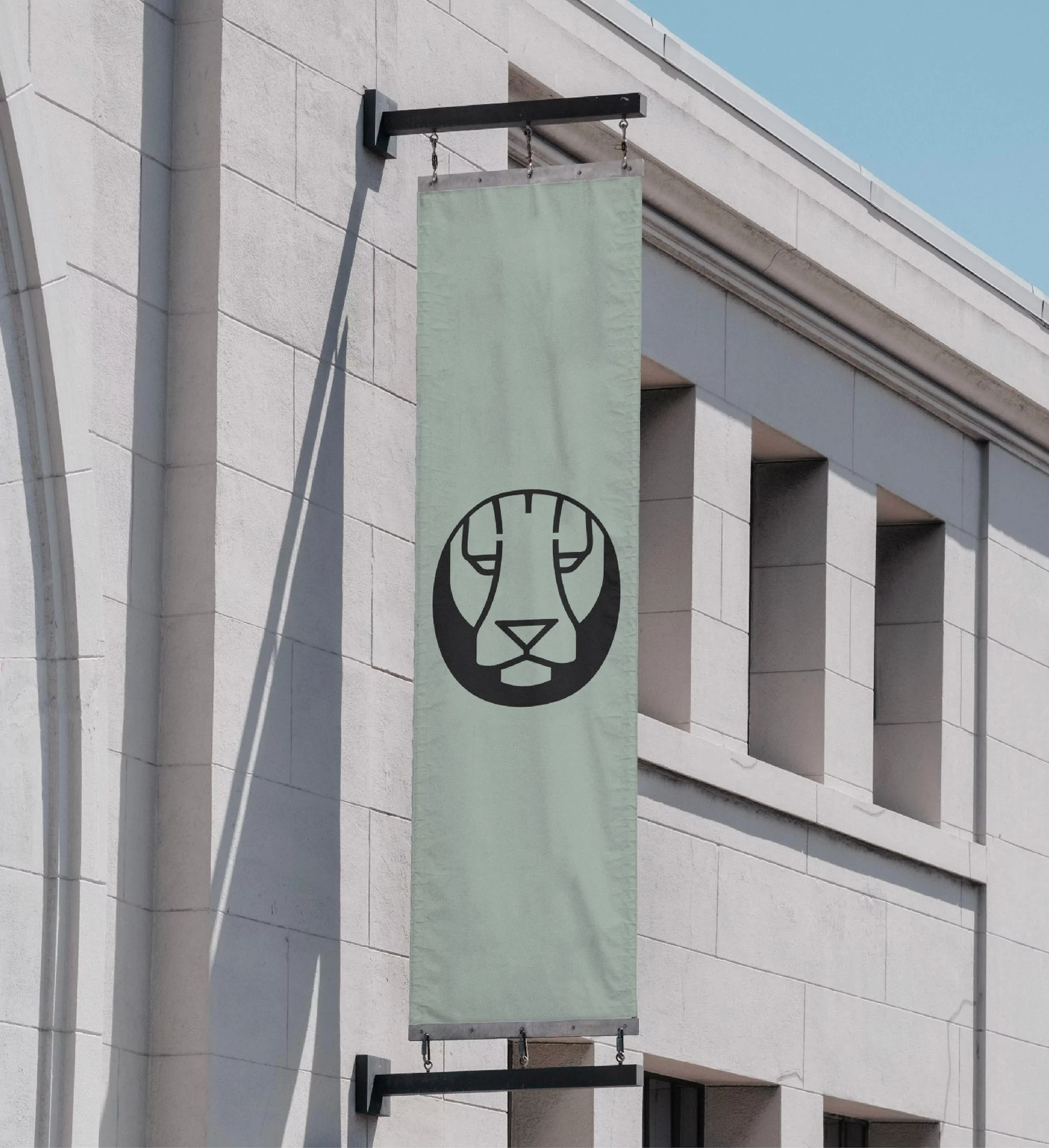 Outdoor shot of a vertical banner hanging on the side of a stone building, displaying a round lion logo against a light green background.