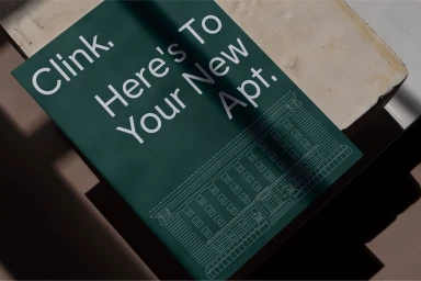 Green branded card with white typography reading Clink. Here's To Your New Apt. resting on a neutral textured surface.