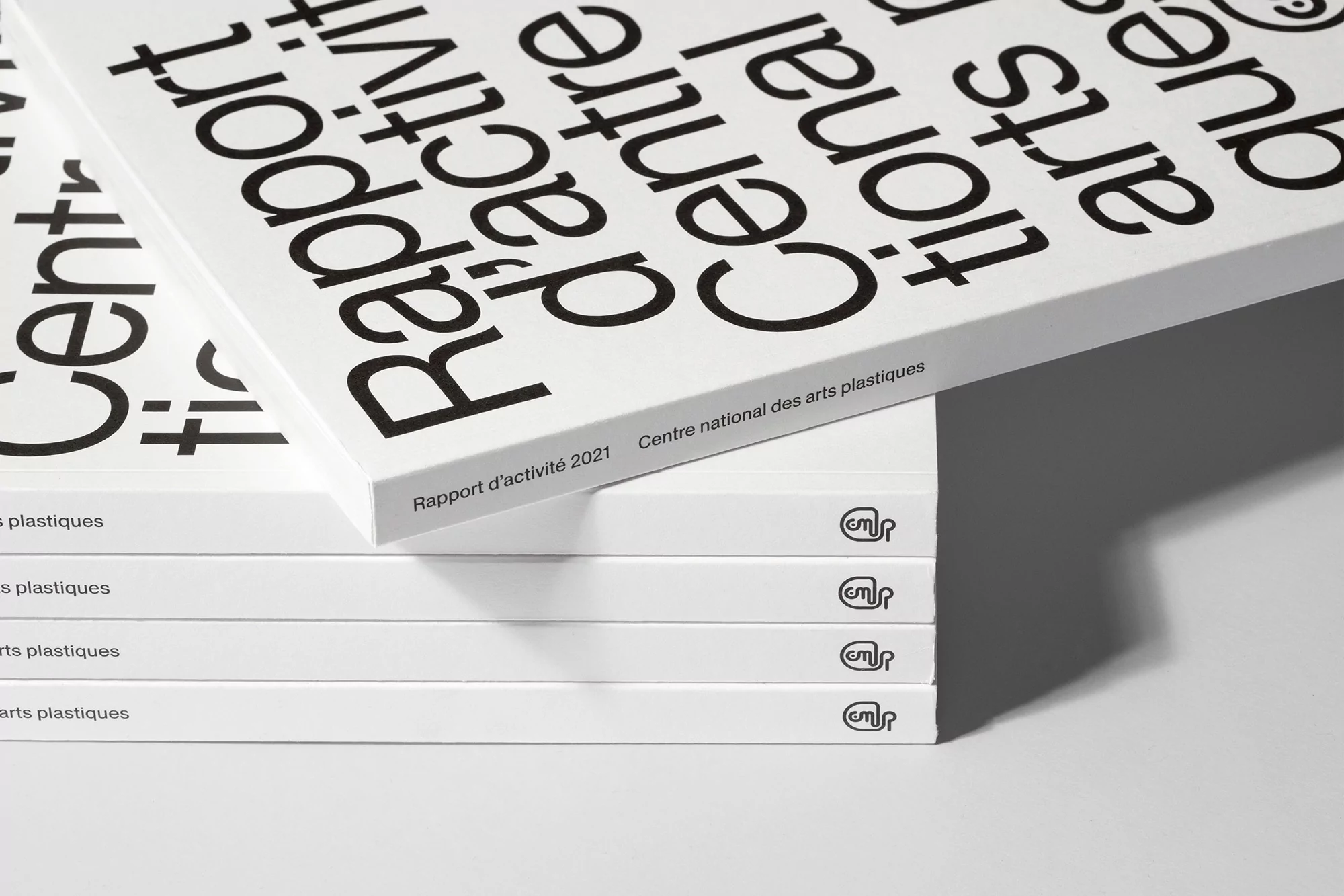 Close-up of a stack of white reports with bold black text, including 'Rapport d'activité 2021' and 'Centre national des arts plastiques'.