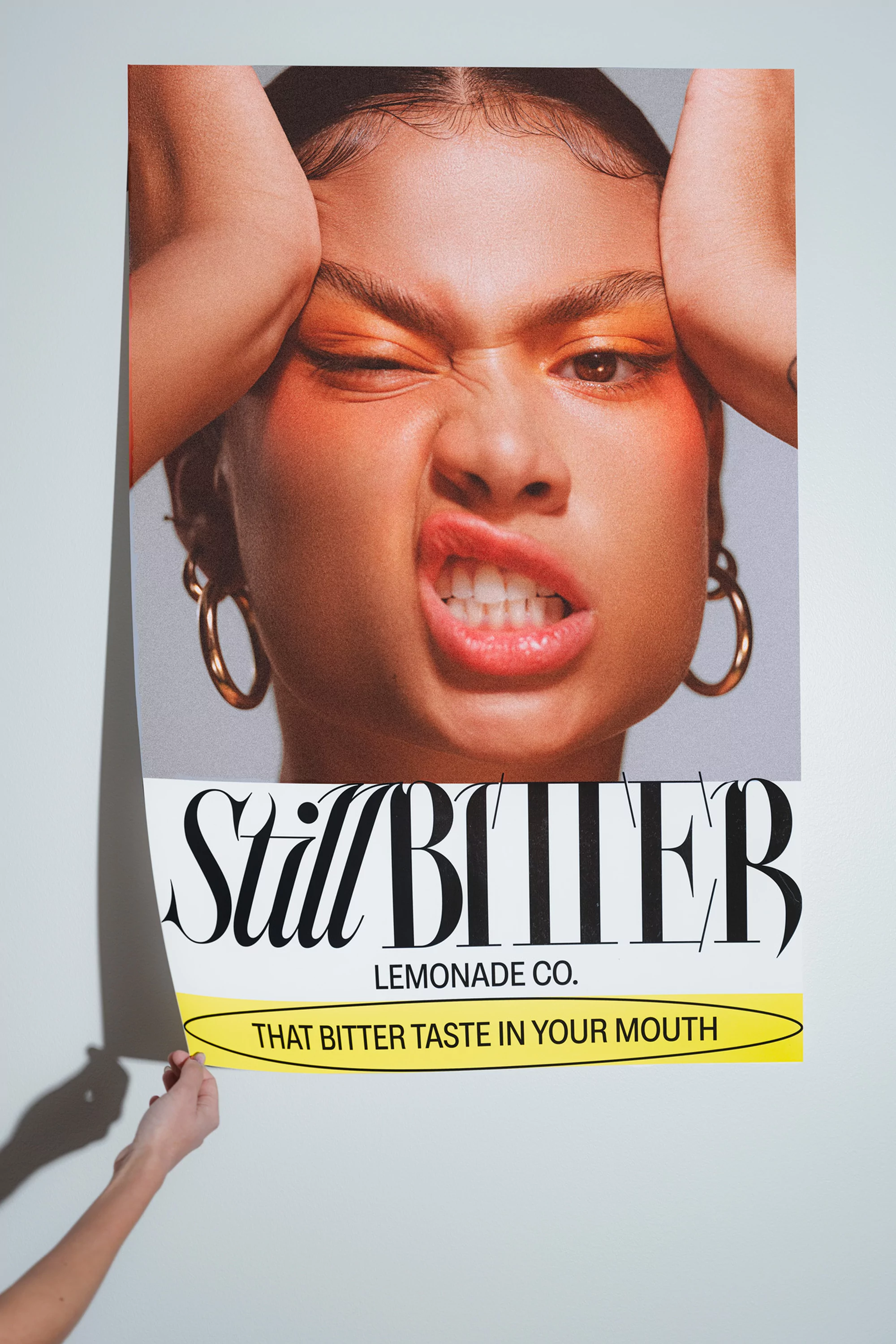 Poster featuring woman with bold makeup and a displeased expression held by person against a light background, promoting Still Bitter Lemonade.