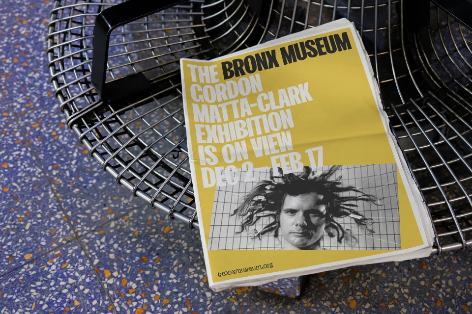 Bronx Museum poster featuring a black and white portrait of Gordon Matta-Clark, displayed on a metal chair on a terrazzo floor.