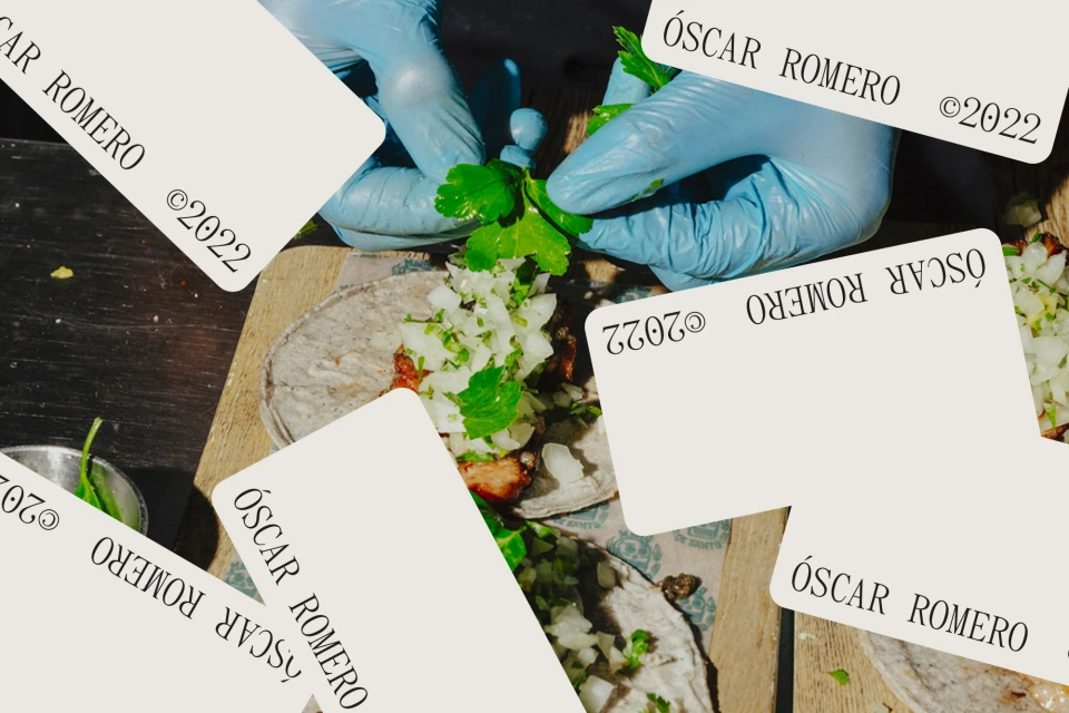 Close-up of tacos being garnished with cilantro by hands in blue gloves, featuring an overhead angle, wooden surface, and bright daylight.