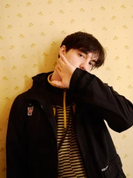 Portrait of young man with dark hair in black jacket and striped top against yellow floral wallpaper