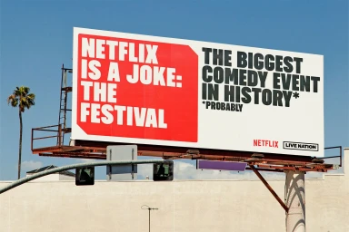 Large outdoor billboard advertising Netflix Is A Joke festival against a clear blue sky with a palm tree on the left