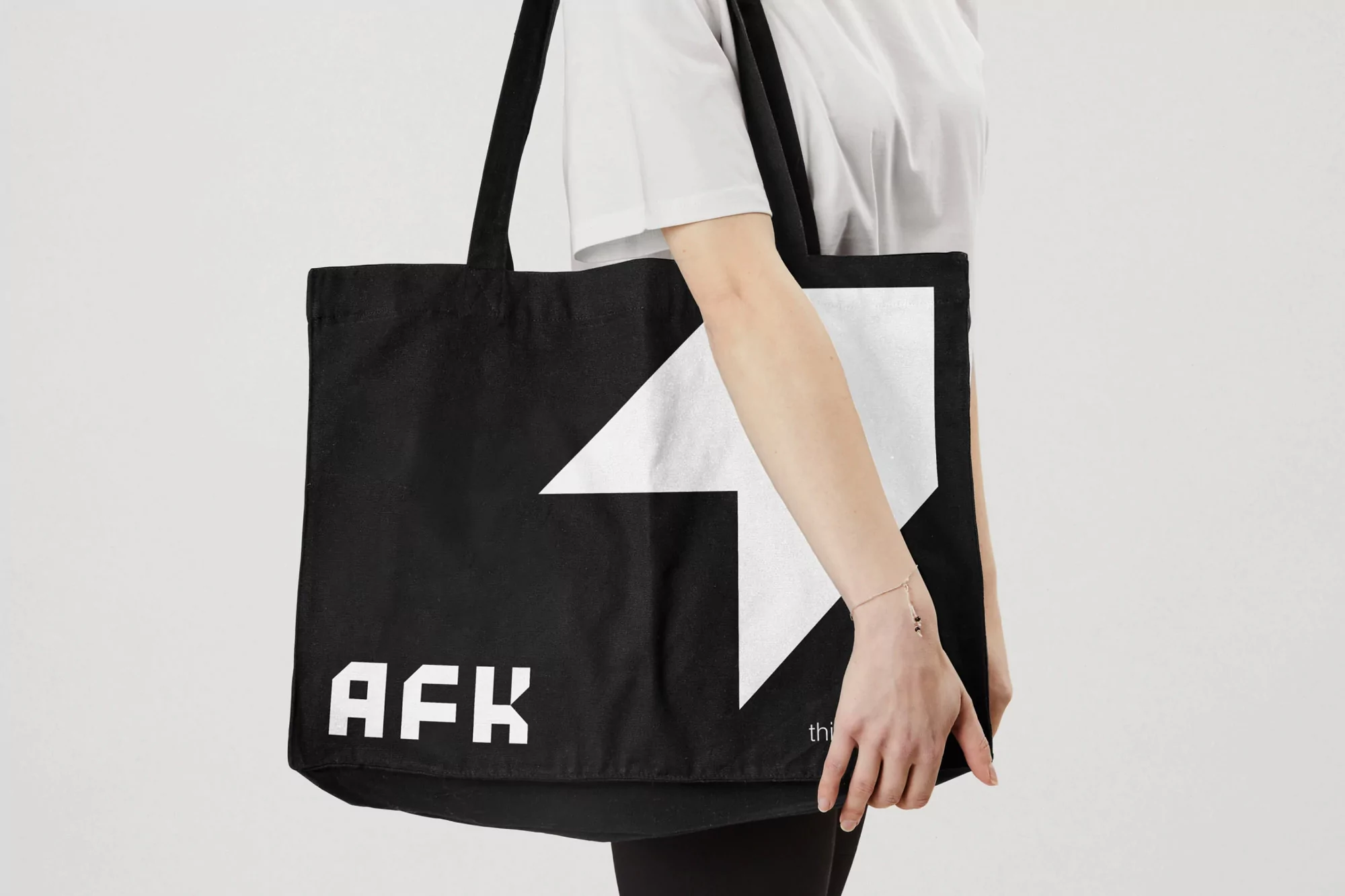 Person displaying a black tote bag with a bold white graphic and the text “AFK”. The background is a solid, neutral tone.