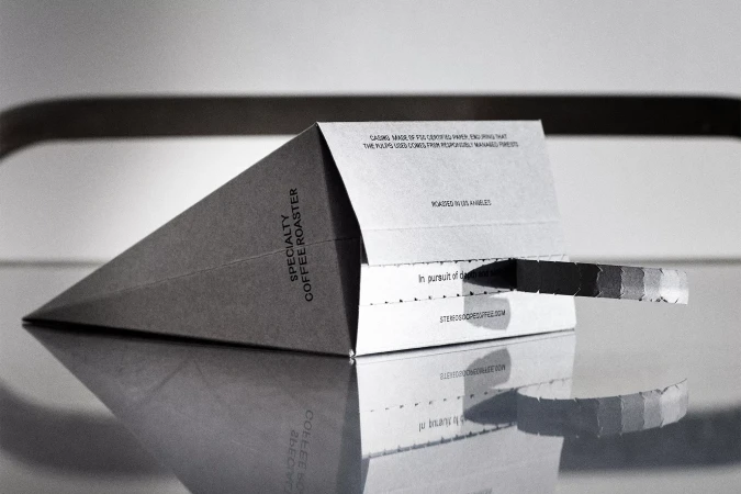 Studio shot of a folded paper coffee bag reflecting on a glossy surface, showcasing sustainable packaging and minimalist product design.