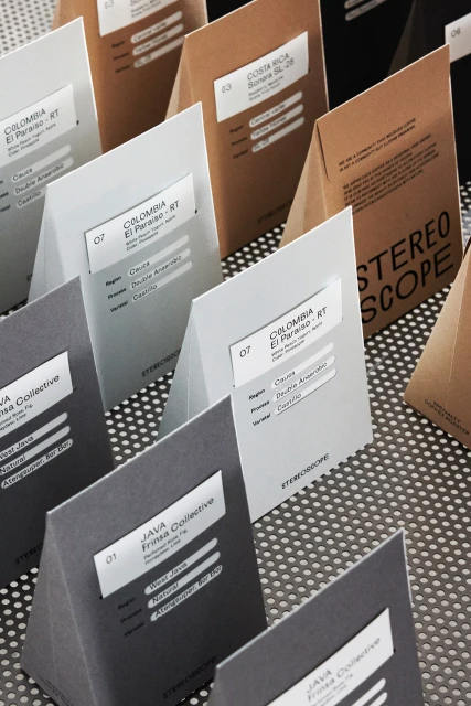 Close-up of triangle-shaped, grey, brown, and white coffee sample packages with labels on a metallic perforated surface.